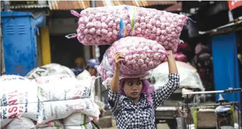  ??  ?? SURABAYA, Indonesia: This picture taken on Thursday shows an Indonesian woman carrying bags of garlic at a market. — AFP