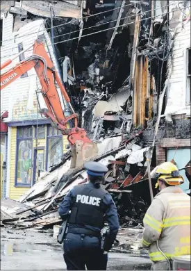  ?? — Photo by Keith Gosse/the Telegram ?? An RNC officer and a St. John’s Regional Fire Department firefighte­r watch as an excavator tears down the front of one of three damaged buildings from Wednesday’s fire on Duckworth Street.