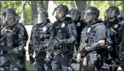  ?? Andy Cross / The Denver Post ?? Aurora police officers in riot gear stand behind a fence monitoring a protest over the death of Elijah Mcclain in police custody that took place outside the Aurora Police Department’s headquarte­rs at the Aurora Municipal Center on June 27, 2020.