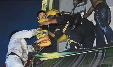  ?? — AP ?? Easy does it: A boy is rescued from the apartment complex during the fire in Ho Chi Minh City.