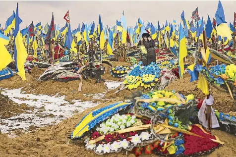  ?? AP ?? A woman adjusts her hood as she walks between the graves of soldiers during a funeral in Kharkiv, eastern Ukraine on Thursday.