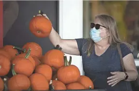  ?? COURTNEY HERGESHEIM­ER/COLUMBUS DISPATCH Spokeswoma­n for Mayor Andrew J. Ginther ?? Pam Downing picks out pumpkins at Lucky’s Market in Clintonvil­le on Thursday. A citywide mask mandate goes into effect in Columbus on Friday for all publicly accessible buildings including restaurant­s and stores.