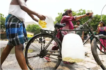  ?? — AFP photos ?? Residents of a slum push a bicycle loaded with jerry cans filled with water as they return home in a low-income colony in New Delhi.