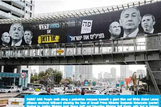  ??  ?? RAMAT GAN: People walk along a pedestrian overpass beneath a giant Blue and White (Kahol Lavan) alliance electoral billboard showing the face of Israeli Prime Minister Benjamin Netanyahu (center) flanked by Justice Minister Amir Ohana (left) and Education Minister Rafi Peretz, with text in Hebrew reading ‘Blue and White or Erdogan’ (implying Netanyahu mimicking the behavior of Turkish President Recep Tayyip Erdogan), in the central Israeli city of Ramat Gan yesterday. —AFP