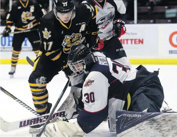  ?? MARK MALONE ?? Spitfires goaltender Lucas Patton tries to get a handle on a loose puck while the Sarnia Sting’s Drake Rymsha tries to score during OHL action Friday in Sarnia. .