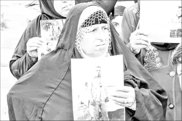  ??  ?? An Iraqi woman holds up a portrait of a missing relative believed to be held captive by IS group fighters.