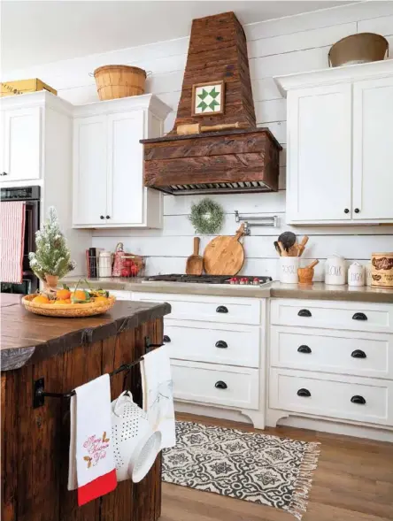  ??  ?? Below: Crafted from antique mushroom wood, the exquisite island and range hood were designed specifical­ly for this kitchen. The eyecatchin­g conversati­on pieces balance white shiplap walls and sleek white cabinetry. Oilrubbed bronze cabinet pulls and an iron towel rack, along with baskets, mashers and other woodenware, complement the rustic aesthetic.