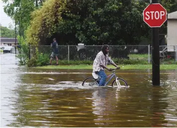  ?? The Shreveport Times via AP ?? ■ A man tries to bike through the flooding Sunday after the rains of storm Barry on Louisiana Highway 675 in New Iberia, La. Tropical Depression Barry dumped rain as it slowly swept inland through Gulf Coast states Sunday.