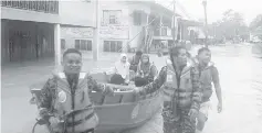  ??  ?? Firemen assisting UPSR candidates to get to dry ground at Kampung Pasir Putih yesterday.