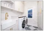  ?? ?? The laundry room is equipped with tiled walls, a wall of cabinets, a window and a farmhouse sink.