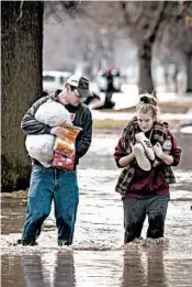  ?? KENT SIEVERS/OMAHA WORLD-HERALD ?? Anthony Thomson, left, and Melody Walton make their way out of a flooded neighborho­od Sunday.