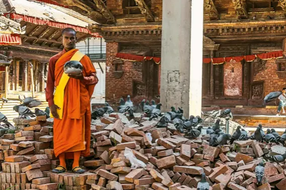 ??  ?? Un călugăr budist așteaptă donații din partea trecătoril­or în celebra Piață Durbar din Kathmandu, afectată de cutremurul din 2015.