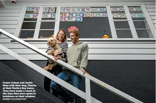  ?? ROBERT KITCHIN/STUFF ?? Fraser Colson and Jackie Shea with their dog, Charlie, at their O¯ whiro Bay home. They have made a count of the days they have spent in lockdown on their window.