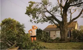  ??  ?? A woman stands in her front yard in Cedar Rapids, Iowa, after the storm, which blew over trees, flipped vehicles, and left thousands without power. Photograph: Andy Abeyta/AP