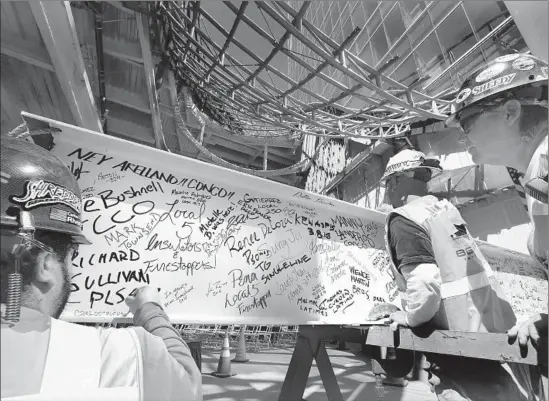  ?? Photog r aphs by Mel Melcon Los Angeles Times ?? GLASS FOREMAN Gary Wahlenmaie­r, right, looks on as glaziers Carlos Riviera, left, and Joe Guevara add their names to a 35- foot, 2,100- pound steel beam.