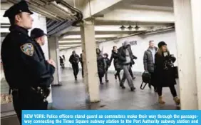  ?? —AFP ?? NEW YORK: Police officers stand guard as commuters make their way through the passageway connecting the Times Square subway station to the Port Authority subway station and bus terminal, near the site of attempted terror attack in New York City.