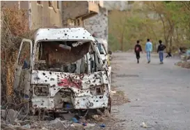  ?? (AFP) ?? Children walk past a shrapnel-ridden vehicle, in Yemen’s rebel-besieged third city of Taez, on Friday