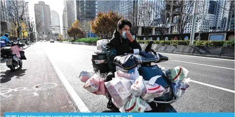  ?? ?? BEIJING: A food delivery man rides a scooter full of orders along a street on Nov 25, 2022. — AFP