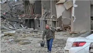  ?? (AFP) ?? A resident carries his belongings as he leaves a damaged building following strikes in Kyiv on Friday.