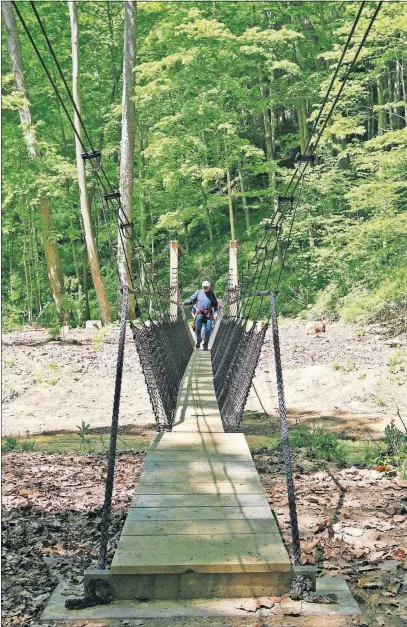  ??  ?? Hiker Larry Long crosses the newly built suspension bridge during the inaugural hike along the Hemlock Bridge Trail at Hocking Hills State Park. The bridge connects the new trails to older gorge trails.