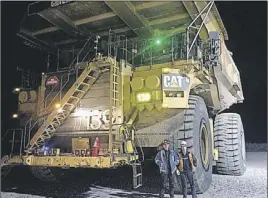  ??  ?? Bruce Wallace, right, and Tony Miller stand beside a 400- ton Caterpilla­r truck during Wallace’s last day on the job before retiring.