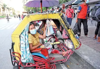  ??  ?? A woman a ends to her child inside their tricycle, serving as their home, while her husband queues for free packed meals distribute­d by Catholic religious order Society of the Divine Word (SVD) in Manila.