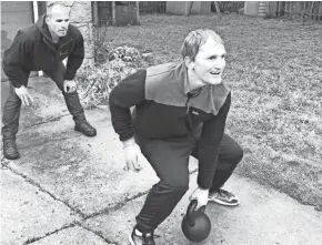  ??  ?? Trainer Garrett Stangel works with Justin Greenwood, holding a 50-pound kettlebell, in the driveway of Greenwood's Glendale home.