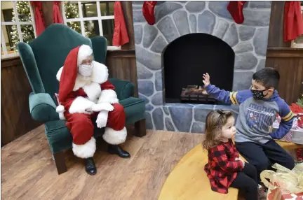  ?? BEN HASTY — MEDIANEWS GROUP ?? Vince Mosqueda, 5, of Exeter Township, waves to Santa while sitting with his sister, Ella, 1 at the Berkshire Mall center court in Wyomissing on Thursday. As a precaution against the spread of COVID-19, Santa wore a mask, and children did not sit on his lap.Vince Mosqueda, 5, of Exeter Township, waves to Santa while sitting with his sister Ella, 1 at the Berkshire Mall Center court in Wyomissing where Santa began visiting with children for Christmas photos Thursday morning December 3, 2020. As a precaution against the spread of COVID-19 Santa wore a mask, and children did not sit on his lap.