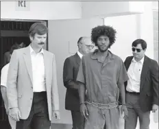  ?? AP PHOTO ?? In this July 31, 1983, file photo, Kevin Cooper (center) a suspect in connection with the slashing death of four people in Chino, is escorted to a car for transport to San Bernadino from Santa Barbara after he was arrested by police at Santa Cruz Island.