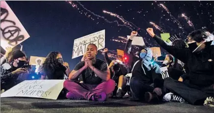  ?? Gina Ferazzi Los Angeles Times ?? FIREWORKS EXPLODE in the background as a protester prays while others rally during a street demonstrat­ion in Santa Ana.