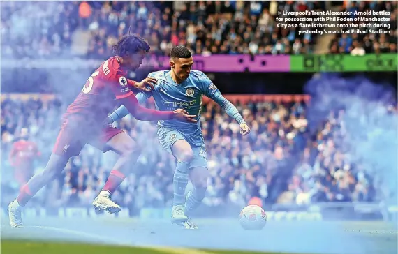  ?? Shaun Botterill ?? > Liverpool’s Trent Alexander-Arnold battles for possession with Phil Foden of Manchester City as a flare is thrown onto the pitch during yesterday’s match at Etihad Stadium