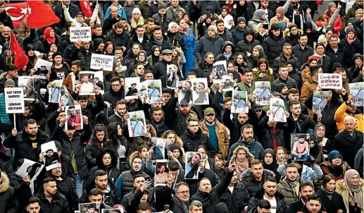  ?? AP ?? People show portrait photograph­s and posters as they take part in a funeral march in Hanau at the weekend. The German language poster reads: ‘‘Assimilati­on policy divides and kills.’’