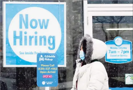  ?? Associated Press ?? A woman walks past a “Now Hiring” sign at a CD One Price Cleaners in Schaumburg, Ill., on Feb. 6. In a stark sign of the economic inequality that has marked the pandemic recession and recovery, Americans as a whole are now earning the same amount of wages and salaries that they did before the pandemic struck, even with nearly 9 million fewer people at work.