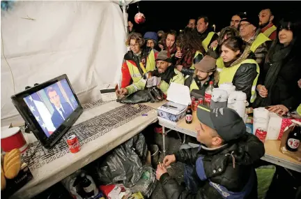  ?? REUTERS ?? PROTESTERS wearing yellow vests watch French President Emmanuel Macron on a TV screen at the motorway toll booth in La Ciotat, near Marseille in this Dec. 10 photo.