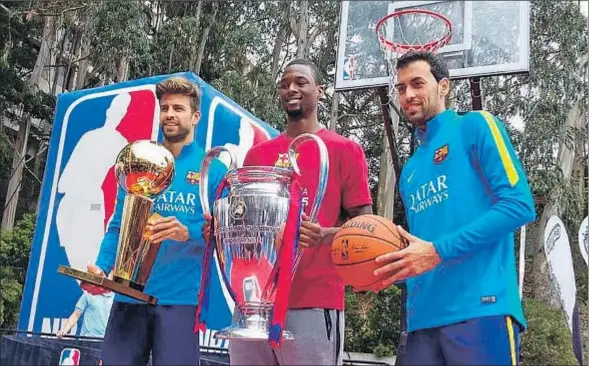  ?? FC BARCELONA ?? Entre campeones. Piqué, que sujeta el trofeo de la NBA, y Busquets, con una pelota de baloncesto, flanquean a Harrison Barnes, campeón de la liga estadounid­ense de baloncesto con los Golden State Warriors