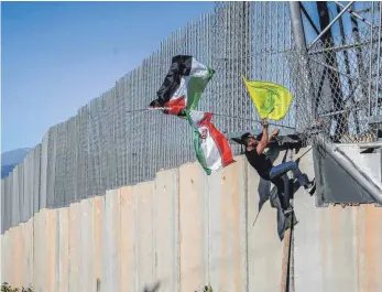  ?? FOTO: MARWAN NAAMANI/DPA ?? Ein Demonstran­t erklimmt den Zaun an der libanesisc­h-israelisch­en Grenze. Die Fahnen weisen ihn als Anhänger der Hisbollah und Irans aus.