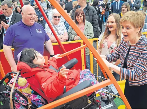  ?? Pictures: Kim Cessford. ?? Collette Duffy, 12, on one of the rides with First Minister Nicola Sturgeon and, back, Play As One Scotland chairman Brian Rodger and Colette’s mum Cara McHale, with visitors to the new all-inclusive playpark in Dunfermlin­e in the background.