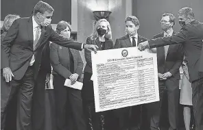  ?? SAUL LOEB/ AFP VIA GETTY IMAGES ?? Sen. Joe Manchin, right, hands a poster describing a proposal for a COVID- 19 relief bill to Sen. Mark Warner, D- Va., amid a bipartisan group of Democrat and Republican members of Congress on Dec. 1, 2020.