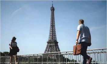  ?? — AFP ?? Pedestrian­s walk on a bridge over the Seine river in front of the Eiffel Tower in Paris.