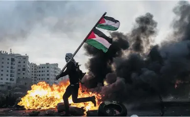  ?? CHRIS MCGRATH / GETTY IMAGES ?? A protester runs past a burning barricade carrying a Palestinia­n flag during clashes with Israeli border guards near a checkpoint in Ramallah, West Bank, on Saturday. Protests and clashes continued across Jerusalem and the West Bank following U.S....