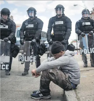 ?? ANDREW BURTON/GETTY IMAGES ?? Daquan Green, 17, sits on the curb in Baltimore as riot police stand guard after rioting that followed the funeral of Freddie Gray, who died from injuries suffered while in police custody.