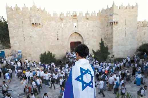  ?? (Reuters) ?? A BOY WRAPPED in an Israeli flag watches as Israelis dance and sing to celebrate Jerusalem Day outside the Old City’s Damascus Gate.