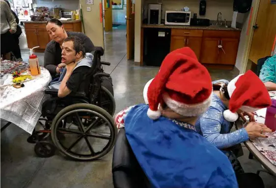  ?? JOHN TLUMACKI/GLOBE STAFF ?? Tyler Bourne (in wheelchair) was assisted by Jade Silva at a Christmas-themed event at Community Connection­s in Mashpee.