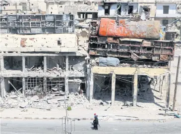  ?? REUTERS ?? People walk past damaged buses positioned atop a building as barricades in the rebel-held Bab al-Hadid neighbourh­ood of Aleppo, Syria, on Thursday.