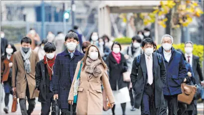  ?? The Associated Press ?? People wearing face masks to help curb the spread of the coronaviru­s walk Monday in a business district in Tokyo. Japanese Prime Minister Yoshihide Suga plans to submit legislatio­n that will make coronaviru­s measures legally binding.