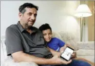  ?? NATI HARNIK — THE ASSOCIATED PRESS ?? In this photo, Hadi Mohammed sits with his 9 year old son Mohammed Ghaleb, as he displays a photo of his son as a baby in Baghdad, in their Lincoln, Neb. apartment. Death threats drove Hadi Mohammed out of Iraq and to a small apartment in Nebraska, where he and his two young sons managed to settle as refugees. But the danger hasn’t been enough to allow his wife to join them.