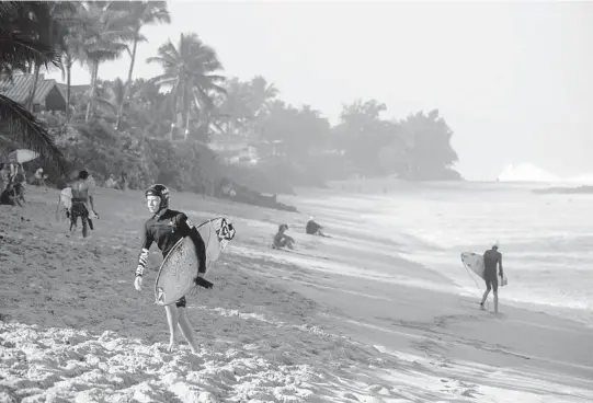  ?? MARIE ERIEL HOBRO/THE NEW YORK TIMES PHOTOS ?? Surfer MaiKai Burdin, wearing a surfing helmet, walks up the beach from the surf Feb. 14 in Haleiwa, Hawaii.