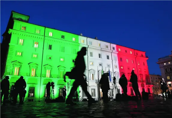  ?? REUTERS ?? Los periodista­s esperan a Conte frente al Palacio Chigi, iluminado con la bandera italiana, ayer