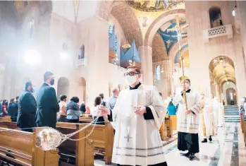  ?? SAUL LOEB/GETTY-AFP ?? With pandemic precaution­s still in place, a priest swings a censer during Easter Mass Sunday at the Basilica of the National Shrine of the Immaculate Conception in Washington. Worshipper­s around the world celebrated.