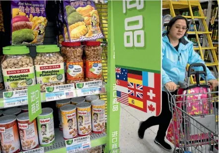  ??  ?? A woman pushes a shopping cart past a display of nuts imported from the United States at a supermarke­t in Beijing. China has announced a list of US goods, including wine, fruit and nuts, that will be hit with higher tariffs in a spiralling trade...